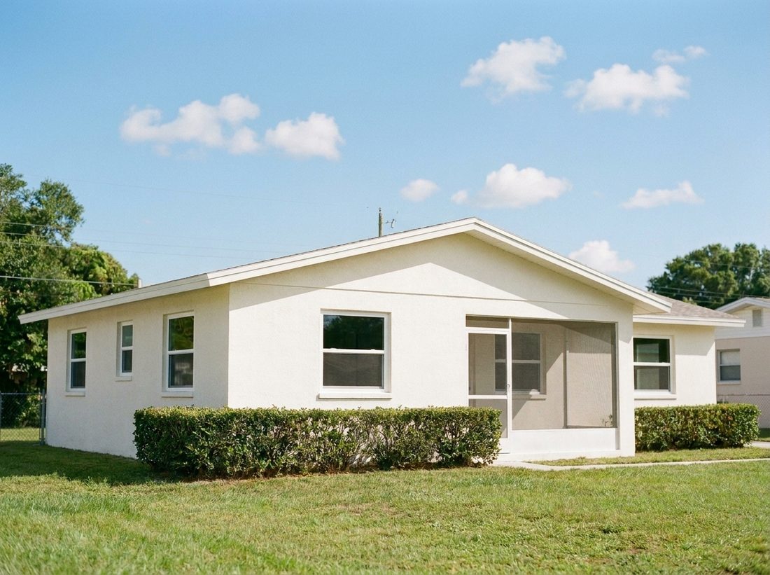 Illustration of the same single story Florida block home on a bright sunny day with new white vinyl impact windows, fresh stucco, and a tidy lawn